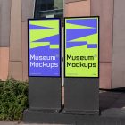 Front view, Two Poster Mockups with purple, black, beige, and neon green geometric designs standing in front of the modern architecture building. Scene from our Museum Mockups product.