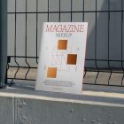 Front view, of outdoor magazine mockups with simple minimalist design in black and red color, serif typography, and square foil pattern resists on metal net fence in black color.