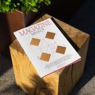 View from above, of outdoor magazine mockups with simple minimalist design in black and red color, serif typography, and diamond foil pattern laying on wooden square.