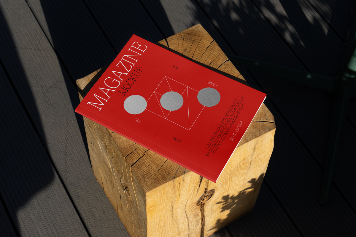 View from above, of outdoor magazine mockups with simple minimalist design in black and red color, serif typography, and circle foil pattern laying on wooden square.