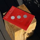 View from above, of outdoor magazine mockups with simple minimalist design in black and red color, serif typography, and circle foil pattern laying on wooden square.