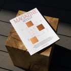 View from above, of outdoor magazine mockups with simple minimalist design in black and red color, serif typography, and square foil pattern laying on a wooden square.