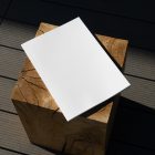 View from above, of a white outdoor magazine mockup laying on a wooden square.