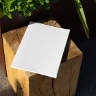 View from above, of a white outdoor magazine mockup laying on a wooden square.