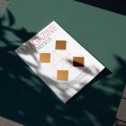 View from above, of outdoor magazine mockups with simple minimalist design in black and red color, serif typography, and diamond foil pattern laying on a green table.