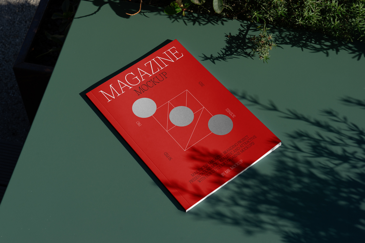 View from above, of outdoor magazine mockups with simple minimalist design in black and red color, serif typography, and circle foil pattern laying on a green table.