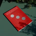 View from above, of outdoor magazine mockups with simple minimalist design in black and red color, serif typography, and circle foil pattern laying on a green table.