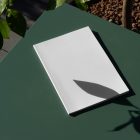 View from above, of a white outdoor magazine mockup laying on a green table.