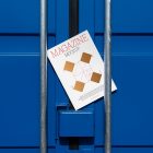 Front view, of outdoor magazine mockups with simple minimalist designs in black and red colors, serif typography, and diamond foil patterns lies between a blue container and a silver metal tube.