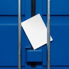 Front view, of a white outdoor magazine mockup lies between a blue container and a silver metal tube.