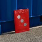 Front view, of outdoor magazine mockups with simple minimalist design in black and red color, serif typography, and circle foil pattern resist on the blue container color.