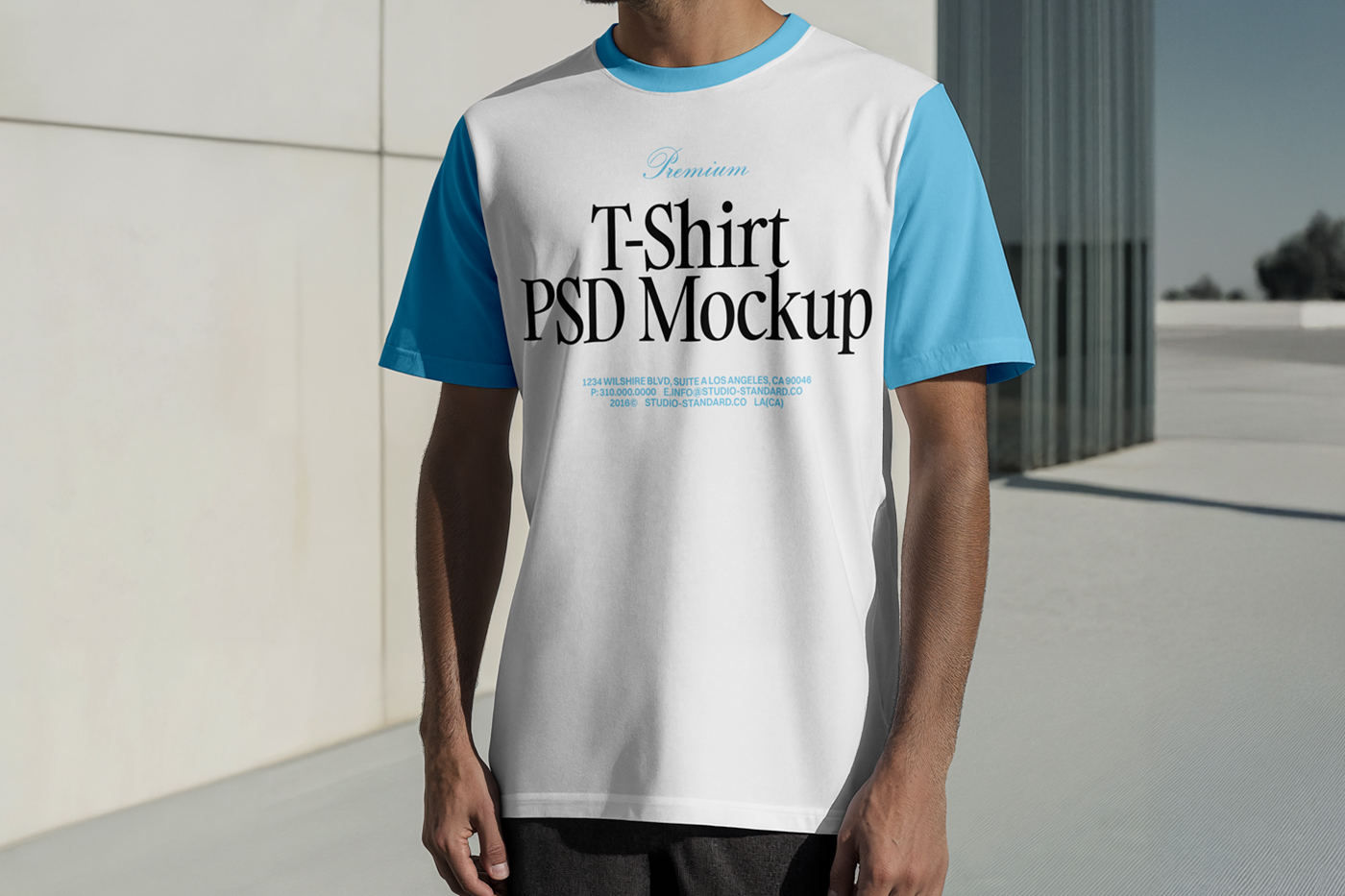 Standing men wearing T-Shirt Mockup with a blue and black logo in front of the white wall.
