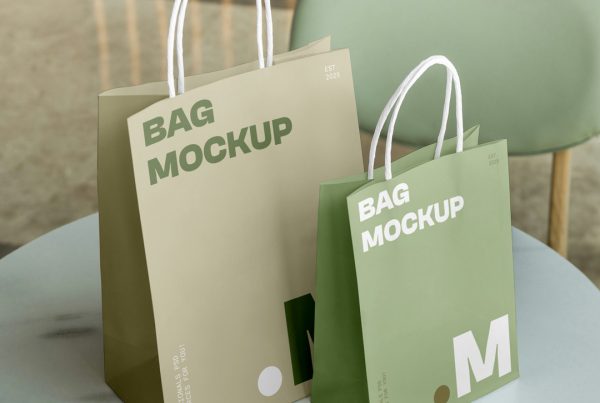 Front view, Two Paper Shopping Bag Mockups with bright gold and green typography design standing on the restaurant marble table.