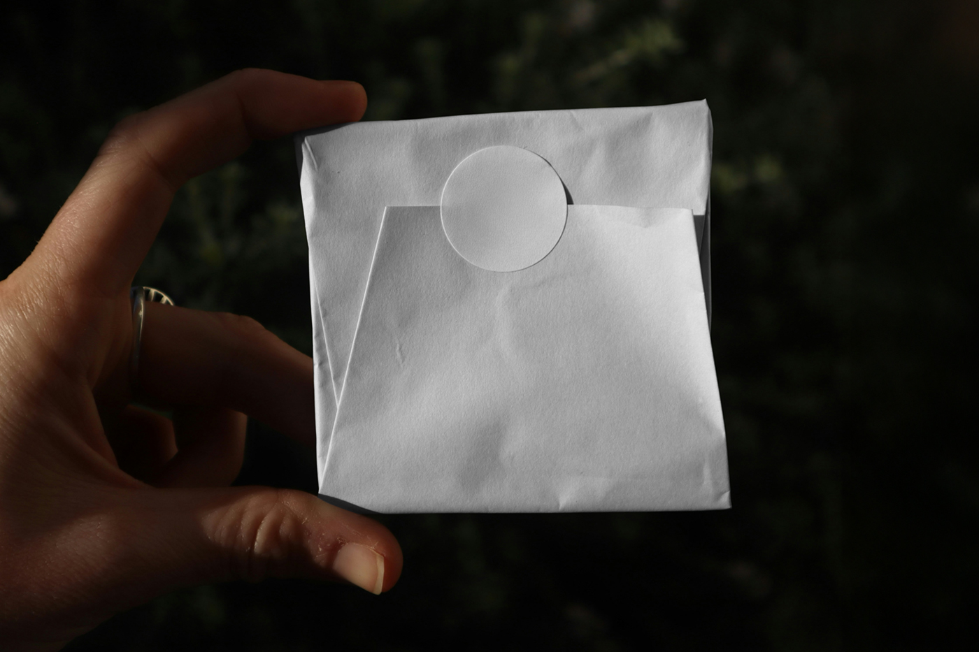 Front view, a White Wrapping Paper Package Mockup with circle sticker against a black background.