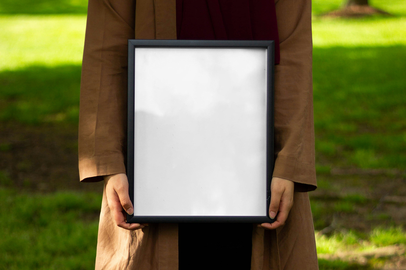 Front view, women holding a framed white poster mockup in their hands against the background of the park.