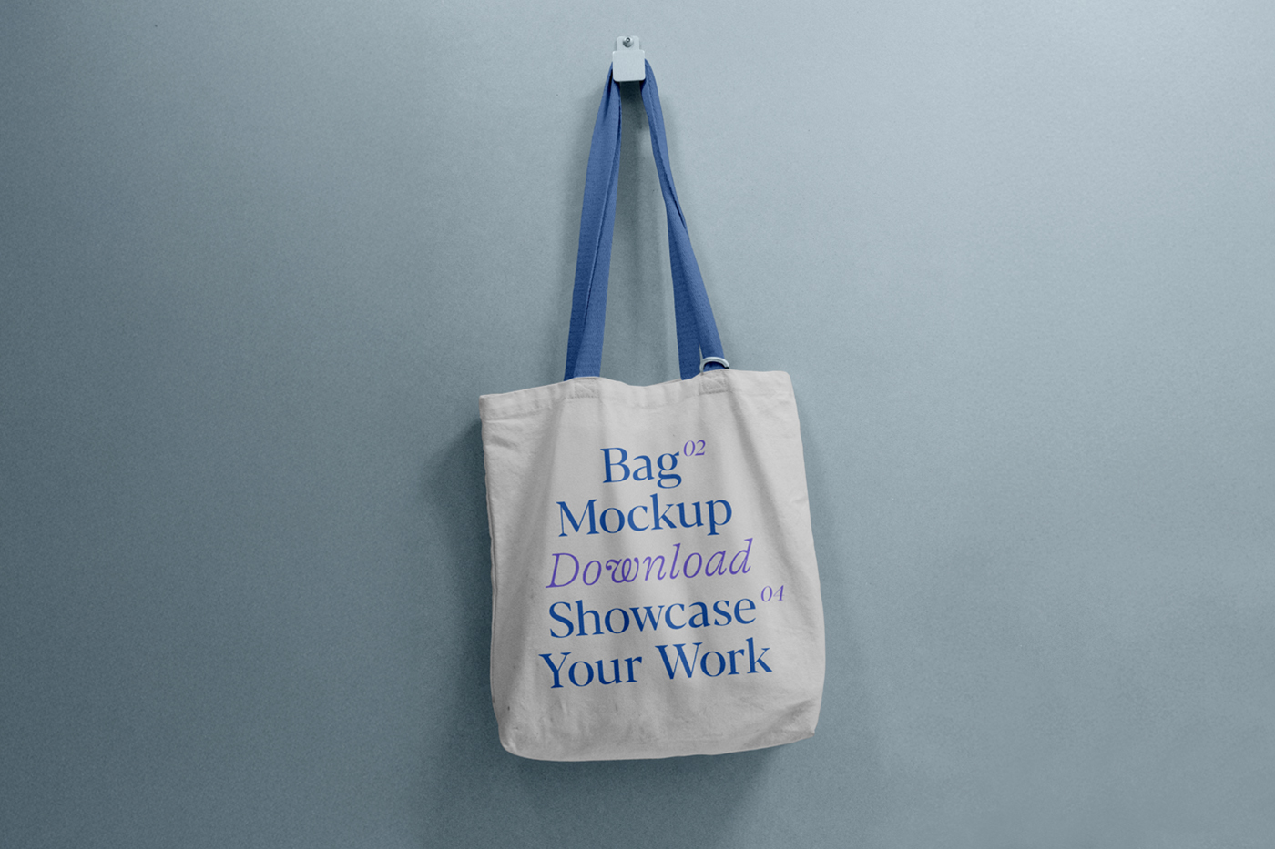 Front view, tote bag mockup with blue and purple typography design hanging on a hook attached to the blue color wall.