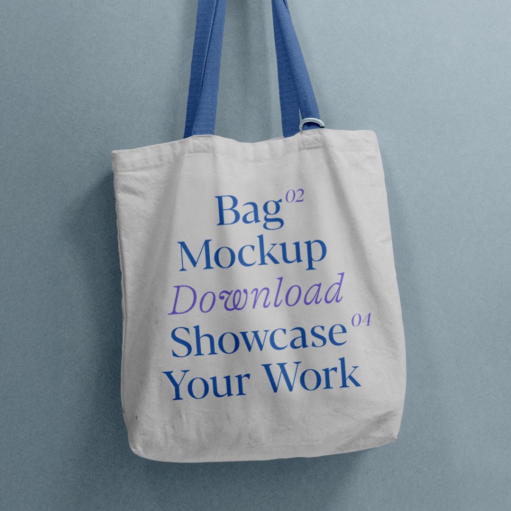 Front view, tote bag mockup with blue and purple typography design hanging on a hook attached to the blue color wall.