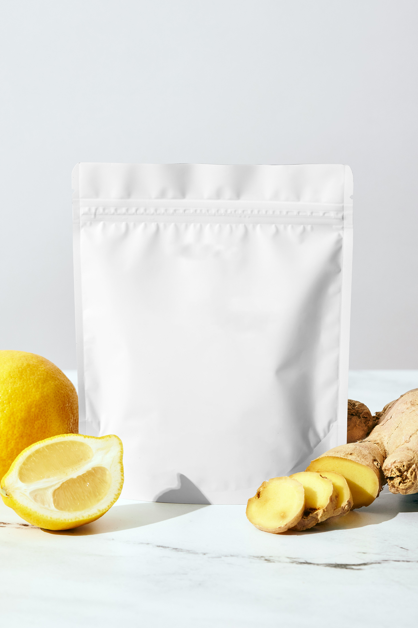 Front view, a white small coffee bag mockup standing on the table between the lemon and ginger.