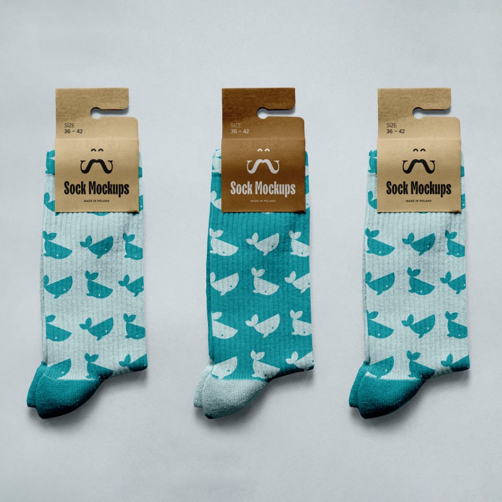 View from above, three socks with craft paper label mockups with simple designs in celadon color lying on a bright blue background color.