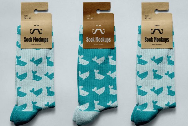 View from above, three socks with craft paper label mockups with simple designs in celadon color lying on a bright blue background color.