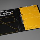 Front view, stationery mockups. Open black binder mockup with white typography design and yellow stroke lines, and a yellow A4 card mockup with black typography and white stroke lines. Everything is lying on a dark gray background.