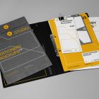 Front view, stationery mockups. Open black binder mockup with a white A4 card mockup and white business card mockup lying on it, strong geometric typography design in yellow, black, and white colors. Everything is lying on a bright gray background.