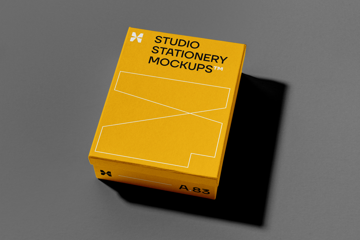 View from above, a yellow box mockup with strong black geometric typography design and white stroke lines. Everything is lying on a dark gray background.