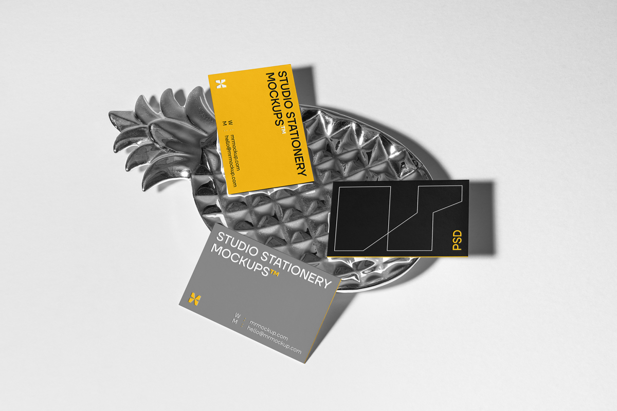 Front view, three business card mockups with strong geometric typography design in white, black, and yellow colors, and also a little geometric sign lying on the background in white color or on a pineapple shaped metal plate in silver color.