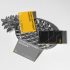 Front view, three business card mockups with strong geometric typography design in white, black, and yellow colors, and also a little geometric sign lying on the background in white color or on a pineapple shaped metal plate in silver color.