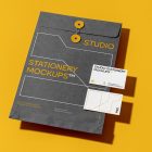 Front view, stationery mockups. Close dark gray envelope mockup with yellow typography and white stroke lines with two white business card mockups lying on it, with a strong black geometric typography design. Everything is lying on a yellow background.