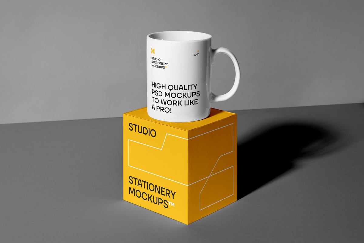Front view, stationery mockups of a yellow square box mockup with strong geometric typography and white stroke lines, and the white cup mockup with strong black typography and the stationery mockups logo placed on it. Everything is lying on a gray background.