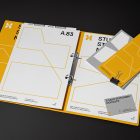 Front view, stationery mockups. Open yellow binder mockup with an white A4 card mockup and gray business card mockups lying on it, strong geometric typography design in yellow, black, and white colors. Everything is lying on a black background.