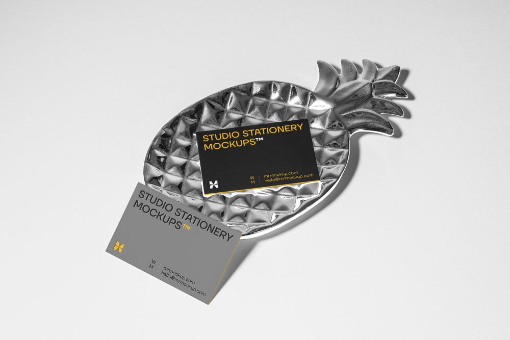 Front view, two business card mockups with strong geometric typography design in black, yellow, and white colors, and also a little geometric sign lying on the background in white color or on a pineapple shaped metal plate in silver color.