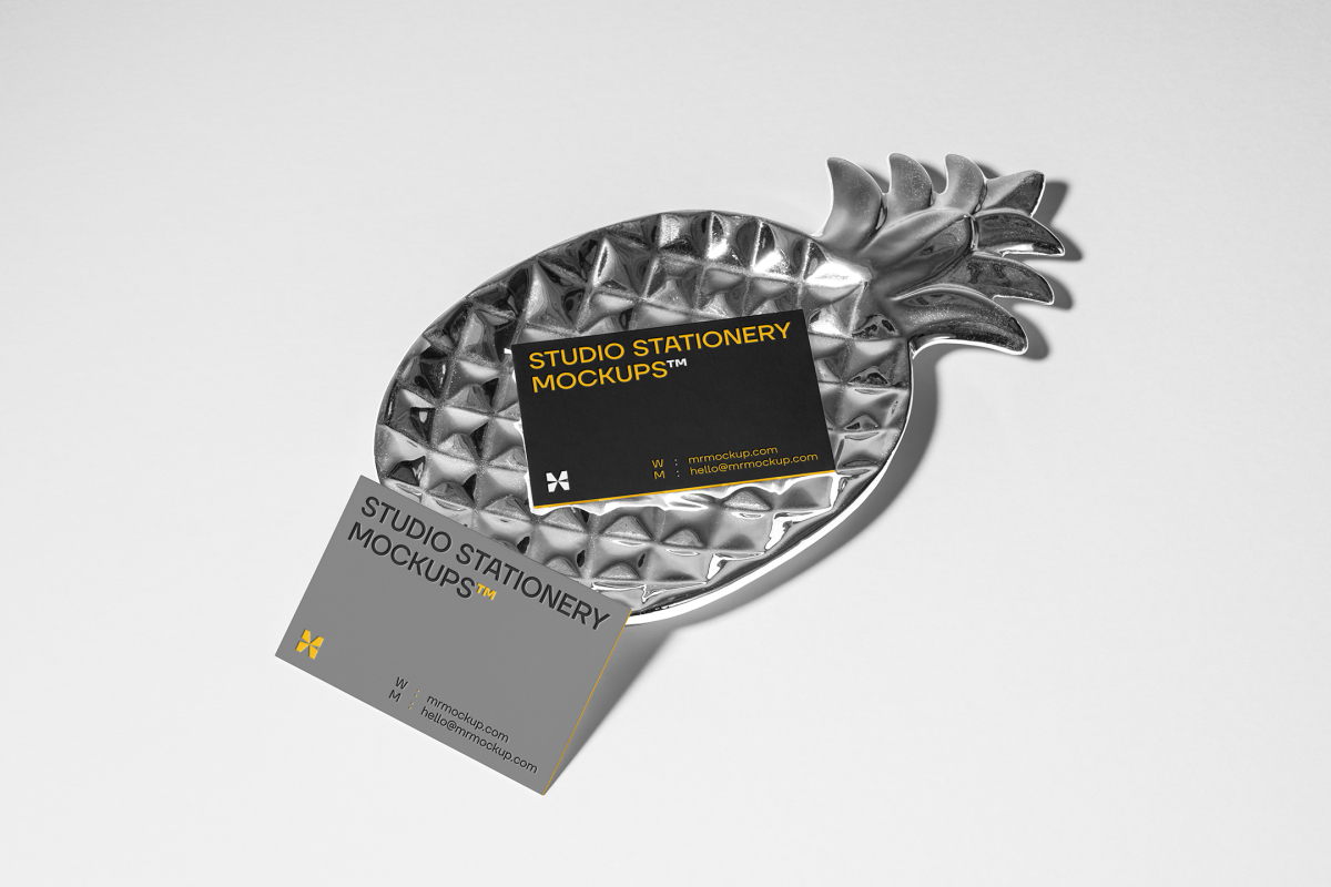 Front view, two business card mockups with strong geometric typography design in black, yellow, and white colors, and also a little geometric sign lying on the background in white color or on a pineapple shaped metal plate in silver color.