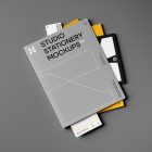 Front view, stationery mockups. A grey folder mockup with a protruding white leaflet mockup, a yellow A4 mockup, and a white business card mockup. Everything is lying on a dark grey background.