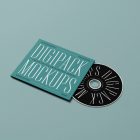Viewed from above, CD Digipack Mockups presents disc packaging and an ejected disc in green and black colors with nice serif typography and 3D graphics lying on the green background.