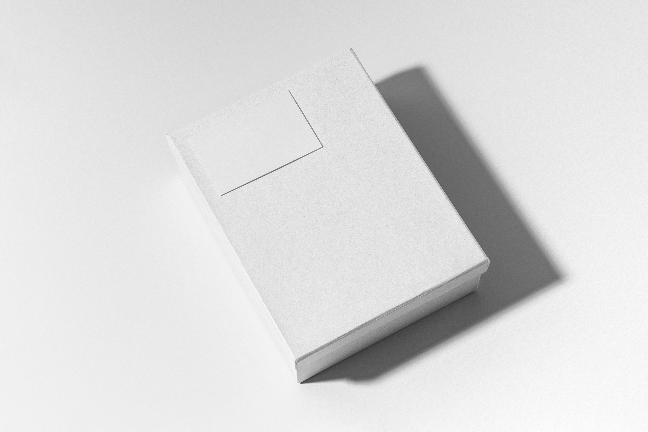 View from above, white box mockup with a visible white business card mockup lying on it. Everything is lying on a white background.