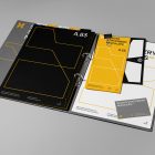 Front view, stationery mockups. Open grey binder mockup with an A4 card mockup, grey business card mockups, yellow leaflet mockup, and black square card mockup lying on it, strong geometric typography design in yellow, black, and white colors. Everything is lying on a bright gray background.
