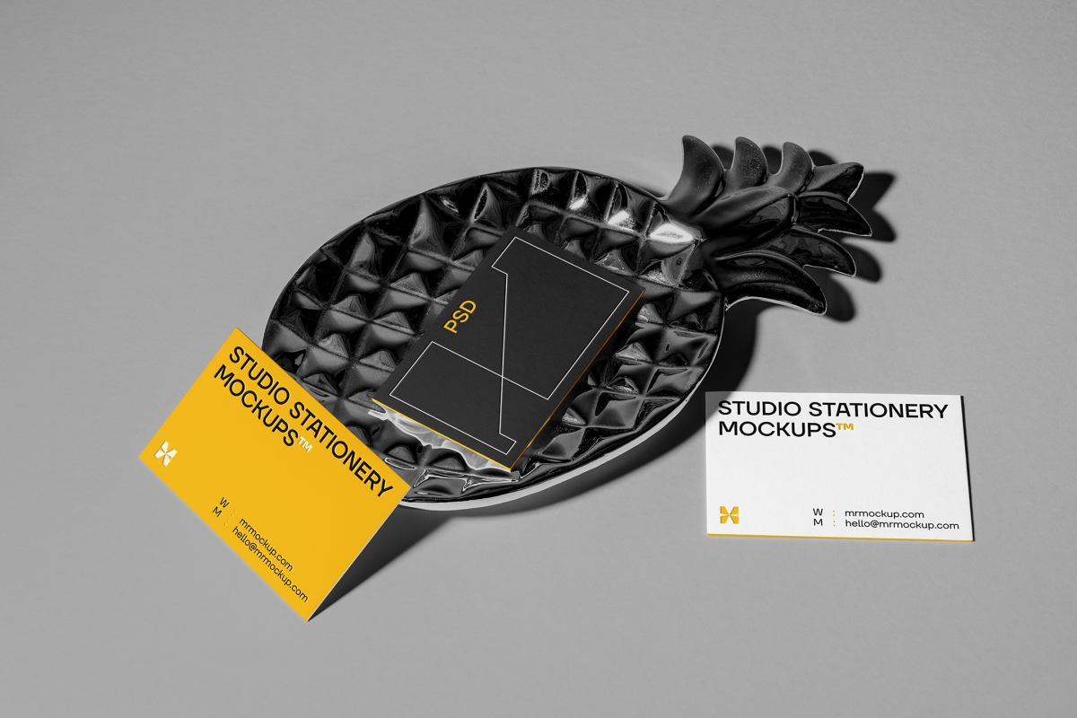 Front view, three business card mockups with strong geometric typography design in white, black, and yellow colors, and also a little geometric sign lying on the background in gray color or on a pineapple shaped metal plate in black color.