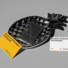 Front view, three business card mockups with strong geometric typography design in white, black, and yellow colors, and also a little geometric sign lying on the background in gray color or on a pineapple shaped metal plate in black color.