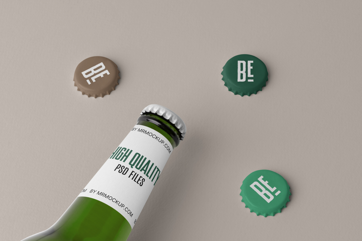 View from above, beer bottle label mockup in white color and black and green typography design with three beer crown caps mockup lying on the beige background.