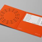 Viewed from above, Vinyl Mockups presents an open music album cover in an orange color with a metal fence graphic and white label with black frames lying on a gray background.