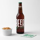 Front view of a standing beer bottle mockup with a white and green typography design, a white peanut container, and a white beer pad mockup with a big green logo standing on the white background floor.