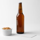 Front view of a standing beer bottle mockup and white peanut container, and a white beer pad mockup standing on the white background floor.