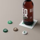 Front view, standing on a white beer pad, beer bottle mockup with white and green typography design, four beer crown cup mockups with white logo design lying on the beige floor.