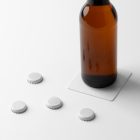 Front view, standing on a white beer pad, beer bottle mockup, four white beer crown cup mockups lying on the white floor.