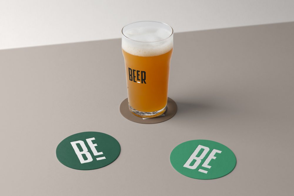 Front view, standing on a brown beer pad, transparent beer glass mockup with black logo design, two green circle beer pad mockups with big white logo design lying on the beige floor.
