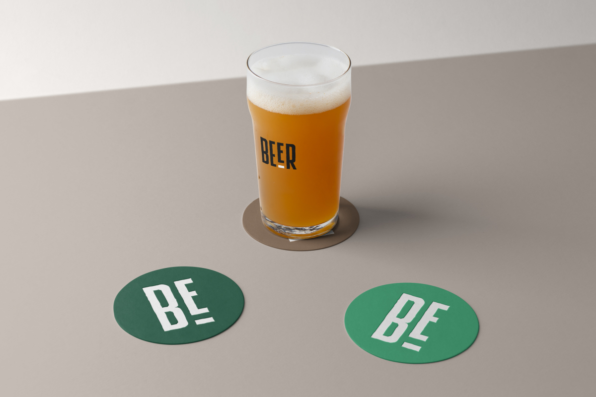 Front view, standing on a brown beer pad, transparent beer glass mockup with black logo design, two green circle beer pad mockups with big white logo design lying on the beige floor.