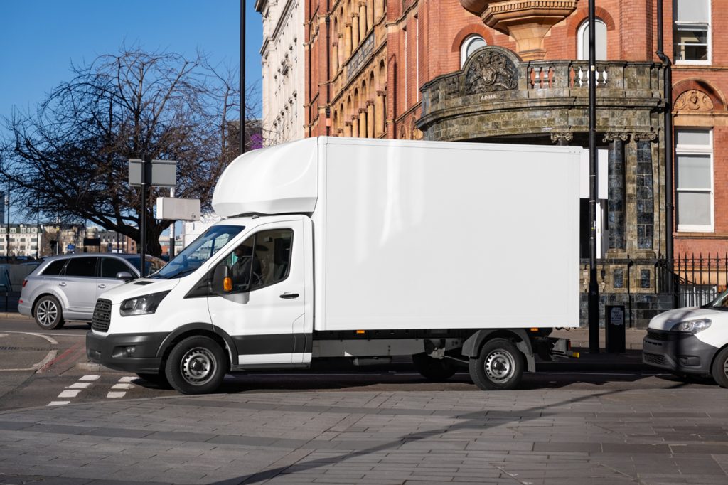 Front view, a white truck mockup stands on the road near the old brick building.