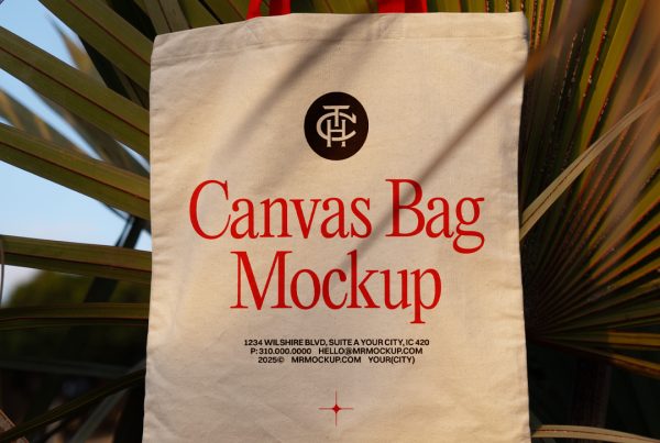 Front view, canvas bag mockup in crème color with a red handle and red and black typography design hanging on the tropical plants.